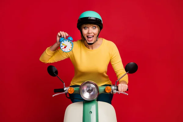 Portret zaskoczony pozytywna dziewczyna rowerzysta kierowca jazdy motocykl rozpocząć wyścigi trzymać niebieski zegar wrażenie krzyczeć wow omg nosić styl stylowy żółty sweter odizolowany jasny kolor tło — Zdjęcie stockowe