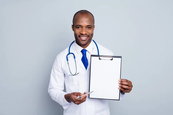 Foto von professionellen Hausarzt dunkle Haut Kerl halten Stift Klemmbrett verschreibungspflichtige Versicherung Apotheke zeigt Ort für Unterschrift tragen Labormantel Krawatte Stethoskop isoliert graue Farbe Hintergrund — Stockfoto