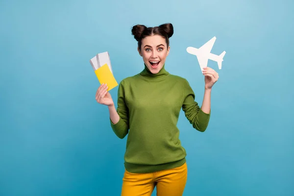 Zdjęcie śmieszne podekscytowany pani trzymać papier samolot samolot bilety uzależniony podróżnik kupić tanie wycieczki za granicą nosić zielony golf żółte spodnie odizolowane niebieski kolor tło — Zdjęcie stockowe
