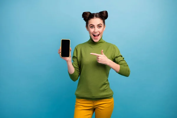 Photo of cheerful excited lady hold new model smart phone present good quality touch screen device open mouth wear green turtleneck yellow pants isolated blue color background