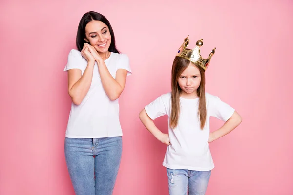 Foto av överlycklig besatt mamma tittar lite arg bortskämd dotter med krona på huvudet imponerad bära casual t-shirts jeans isolerad pastell rosa färg bakgrund — Stockfoto