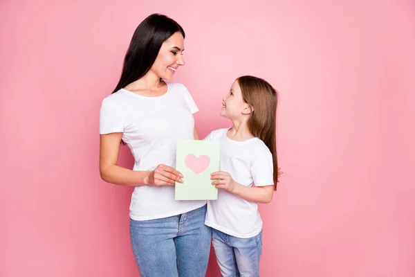 Foto av ganska ung mamma lilla dotter hålla 8 Mars vykort hjärta känslor kramar ser ögon bära casual t-shirts jeans isolerad pastell rosa färg bakgrund — Stockfoto