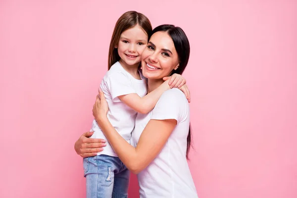 Foto av vackra unga mamma hålla armar kramar lilla dotter gott humör bästa vänner vackra uppriktiga känslor bära casual t-shirts jeans isolerad pastell rosa färg bakgrund — Stockfoto