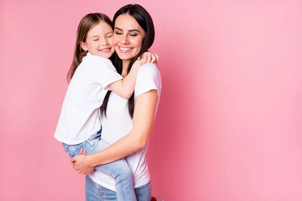 Photo of beautiful young mother hold arms little daughter two ladies hugging best friends lovely feelings eyes closed wear casual t-shirty jeansy odizolowany pastelowy różowy kolor tła — Zdjęcie stockowe