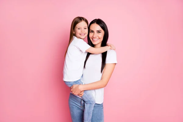 Photo of beautiful young mother hold arms little daughter two ladies hugging good mood best friends wear casual white t-shirts jeans isolated pastel pink color background — Stock Photo, Image