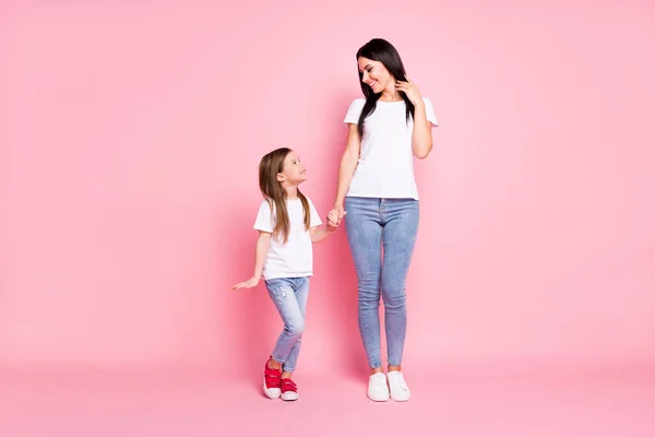 Foto de comprimento total de atraente jovem mãe pequena filha bom humor melhores amigos segurar braços olhar olhos usar casual branco t-shirts jeans isolado pastel cor rosa fundo — Fotografia de Stock