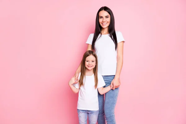 Photo de attrayante jeune maman mère petite fille deux dames de bonne humeur stand proches meilleurs amis tenir bras porter casual blanc t-shirts jeans isolé couleur rose pastel fond — Photo