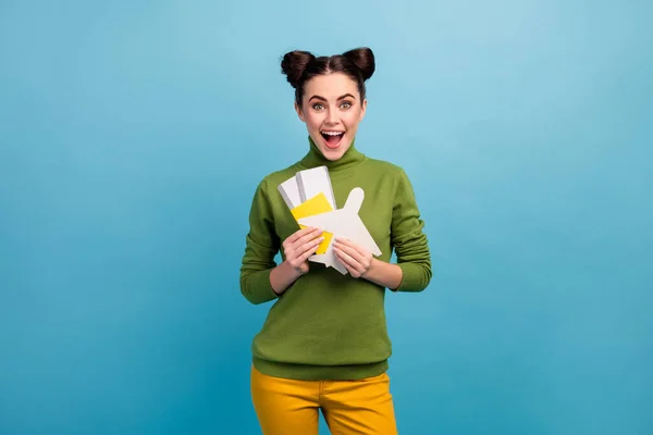 Photo of pretty funny lady hold paper air plane passport tickets addicted traveler buy cheap tour abroad wear green turtleneck yellow trousers isolated blue color background — Stock Photo, Image