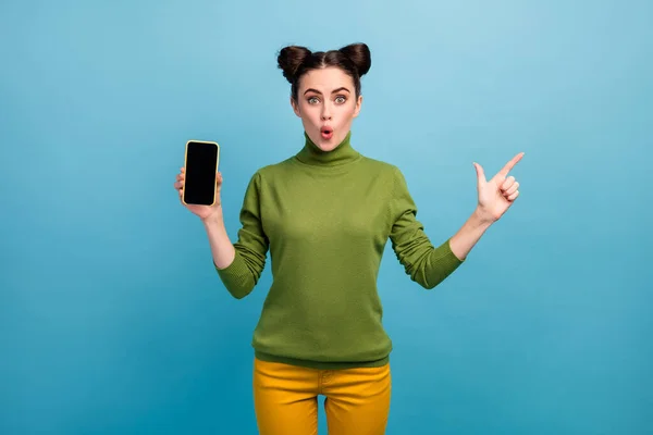 Фото красивої леді менеджер продажів тримає нову модель смартфона прямий палець збоку порожній простір відкритий рот носити зелені черепашки жовті штани ізольовані синій колір фону — стокове фото
