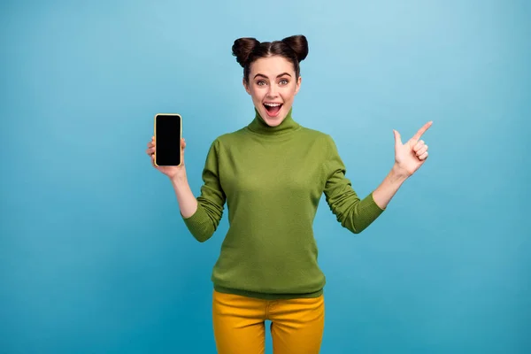Фото смішної красивої леді менеджер продажів тримає нову модель смартфона пристрій прямий палець збоку порожній простір носити зелені черепашки жовті штани ізольовані синій колір фону — стокове фото