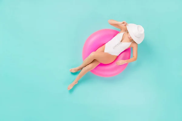 Yüksek açılı, üst açılı, zarif, bronz tenli, yüzme havuzunda oturan bir kadının fotoğrafı. Büyük bir şamandıra. Güneş şapkalı, beyaz yüzme tulumu giyin. — Stok fotoğraf