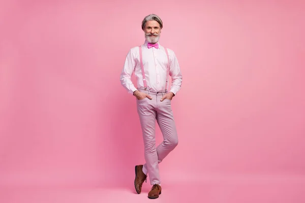 분홍색 파스텔 색상 배경에 고립된 주머니에 손을 잡고 있는 회색 머리의 남자. — 스톡 사진