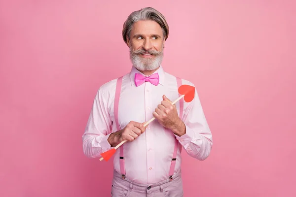 분홍색 파스텔 색상 배경으로 고립된 손에 화살을 들고 있는 회색 머리의 멋진 남자의 모습 — 스톡 사진