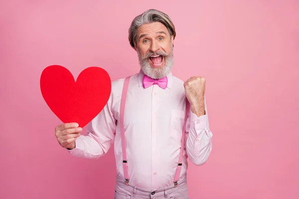 밝고 명랑 한 회색 머리의 남자가 분홍색 파스텔 색 배경 위에 고립된 성인식을 축하하는 대규모 심장을 손에 들고 있는 그 의 매력적 인 모습 — 스톡 사진