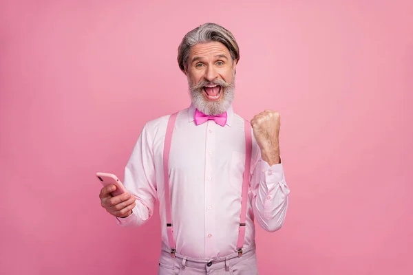 Retrato de su agradable atractivo imponente alegre alegre alegre alegre hombre de pelo gris utilizando la célula celebrando el éxito ganar aislado sobre fondo de color pastel rosa —  Fotos de Stock