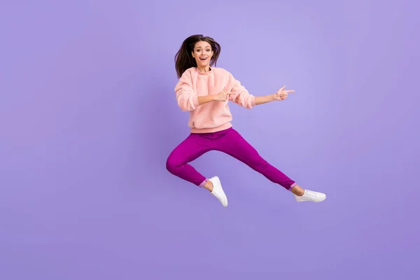 Foto de comprimento total de senhora alegre pulando alto indicando dedos espaço vazio incrível venda desgaste casual fofo pulôver calças sapatos isolado cor roxa fundo — Fotografia de Stock