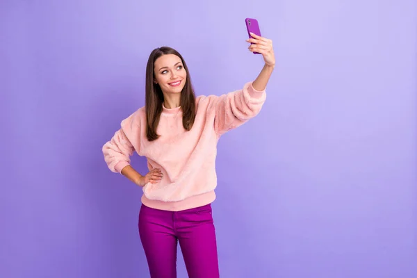Фото смешной девушки молодой держать телефон делает селфи популярный блог онлайн перевод носить случайный пушистый свитер брюки изолированный фиолетовый цвет фона — стоковое фото