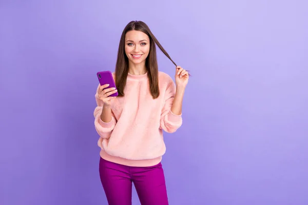 Zdjęcie dość blogger pani trzymając telefon ręce smsowanie przyjaciele bawiąc się z długimi curl nosić casual futro puszyste miękkie pullover spodnie odizolowane fioletowy kolor tła — Zdjęcie stockowe