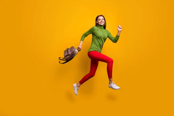 Foto de perfil de cuerpo completo de la señora bonita funky saltando alto sosteniendo el bolso joven fresco corriendo a casa después de estudiar desgaste casual verde jersey pantalones rojos aislado color amarillo fondo —  Fotos de Stock