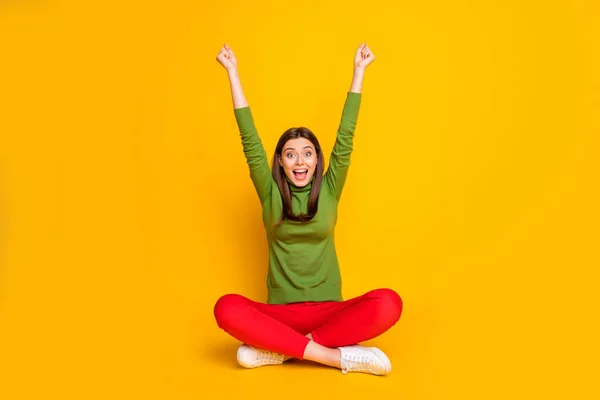 Photo of beautiful lady sit floor holding fists raised supporting favorite sports team excited cheery mood wear green sweater red trousers isolated yellow color background — Stock Photo, Image