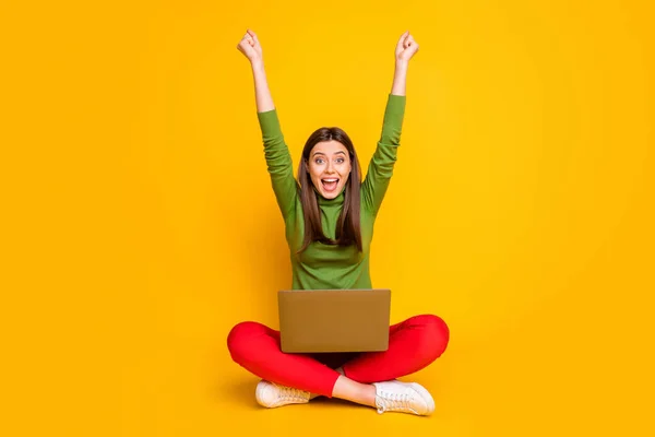 Foto der schönen Dame sitzen Boden lesen Notizbuch Online-Tabelle mit Prüfungsergebnissen feiern beste Note heben Fäuste tragen grünen Pullover rote Hose isoliert gelbe Farbe Hintergrund — Stockfoto