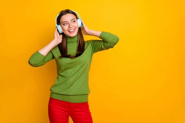 Foto der schönen Dame hält die Hände auf den Ohren Urlaub Zeit hören Jugendmusik suchen Seite leer Raum tragen coole Ohrenklappen grün Pullover rote Hose isoliert gelbe Farbe Hintergrund — Stockfoto
