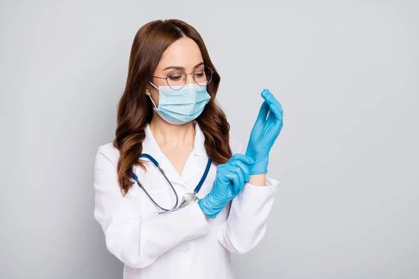 年轻的专业外科医生戴上乳胶手套，戴着防毒面具，听诊器白色实验室外套，隔离灰色背景 — 图库照片