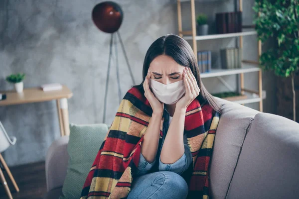 Foto de chica frustrada sufren de migraña terrible toque manos frente tienen corona virus síntoma manta a cuadros cubierta cuerpo estancia en casa llevar máscara respiratoria sentarse sofá en casa en interiores — Foto de Stock