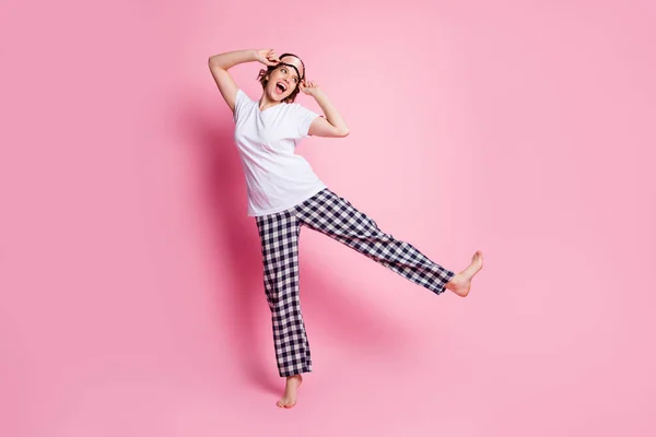 미녀가 다리를 치켜올리고 기분좋은 밤샘 파티를 하는 모습, 비어 있는 공간에 는 수면 마스크 흰색 티셔츠 체크무늬 파자마 바지, 핑크 색 배경 이 따로 있다. — 스톡 사진