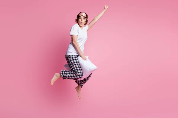 Ganzes Foto von lustigen verrückten Dame springen hohes Kissen zwischen den Beinen Flug voran tragen Schlafmaske weißes T-Shirt karierte Pyjamahose barfuß isoliert rosa Farbe Hintergrund — Stockfoto