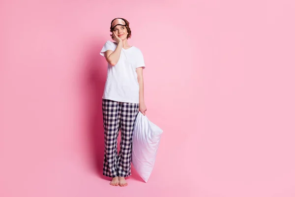 Foto de comprimento total de bela senhora segurar travesseiro olhar para o espaço vazio sonhador bom humor usar máscara de sono branco t-shirt xadrez calças pijama descalço isolado cor rosa fundo — Fotografia de Stock