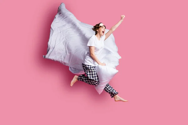 Full body profile photo of funny lady jump high pillow between legs blanket flight moving ahead wear sleep mask white t-shirt plaid pajama pants barefoot isolated pink color background