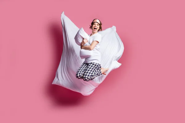 Полная длина фото веселой леди прыгать высокие объятия подушки одеяло полета девушки ночь носить маску для сна белая футболка клетчатая пижама брюки босиком изолированный розовый цвет фона — стоковое фото