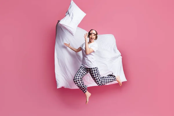 Full storlek foto av rolig dam hoppa högt kast kudde upp filt flygning glädje slummer parti bära sömn mask vit t-shirt rutig pyjamas byxor barfota isolerad rosa färg bakgrund — Stockfoto