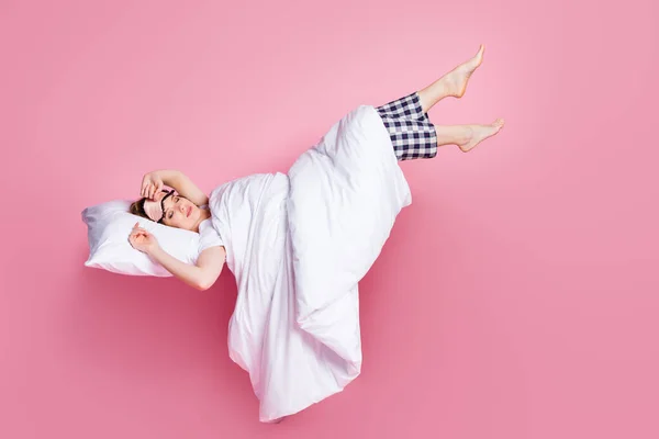 Foto de tamaño completo de la bella dama sábados siesta acostada cama almohada manta dormir y caminar levantar las piernas espacio vacío usar máscara blanca camiseta pantalones de pijama descalzo aislado color rosa fondo —  Fotos de Stock