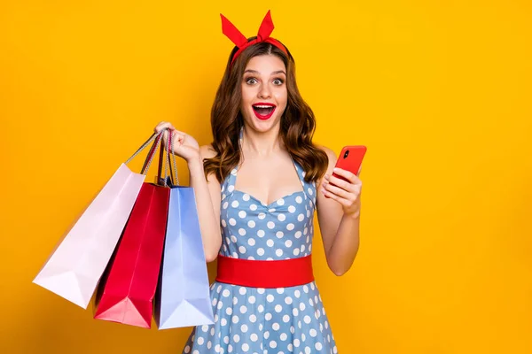 Stupito sorpreso centro commerciale cliente ragazza uso smartphone sfogliare occasioni off-sale urlo wow omg tenere borse indossare blu punteggiato vestito rosso retro fascia isolata lucentezza giallo colore sfondo — Foto Stock