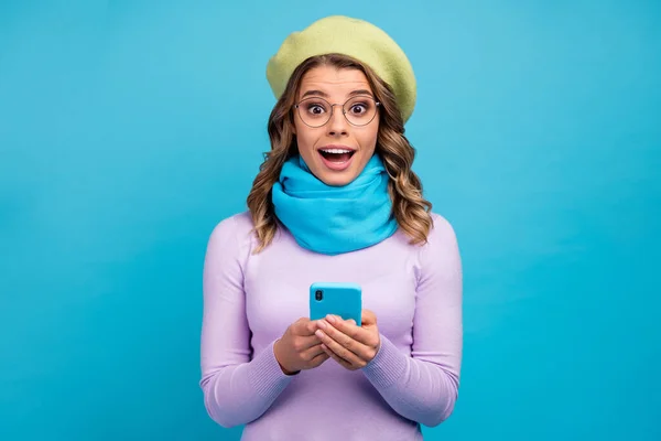 Porträt von erstaunt aufgeregt verrücktes Mädchen verwenden Smartphone beeindruckt Social Network Benachrichtigung schreien wow omg tragen trendige violette Pullover grüne Kopfbedeckung isoliert über blauem Hintergrund — Stockfoto