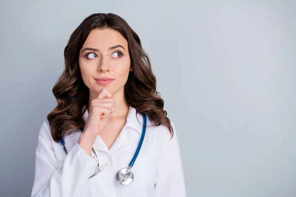 Photo of attractive family doc lady patients consultation virology clinic look side empty space interested hand on chin wear white lab coat stetoskop odizolowany szary kolor tła — Zdjęcie stockowe