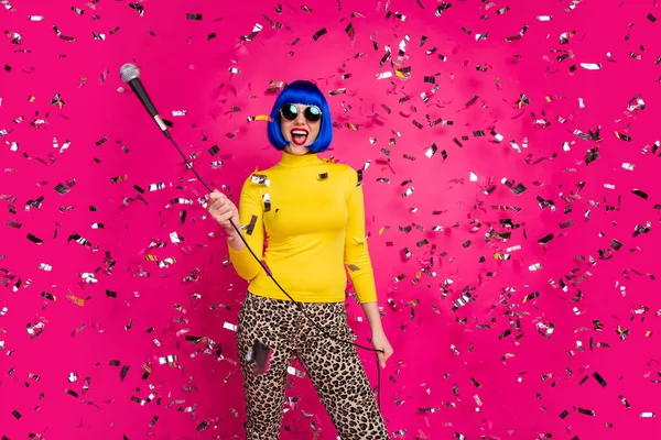 Fotografie vzrušený krásná dáma strana noc klub držet mikrofon zpívat karaoke konfety podzim nosit brýle žluté rolák modrá paruka leopard kalhoty izolované živé růžové barvy pozadí — Stock fotografie