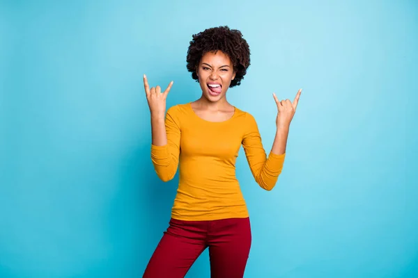 Retrato de fresco loco funky adolescente afro americana chica hacer con cuernos símbolo disfrutar de heavy metal concierto lengua fuera mueca cara desgaste elegante jersey rojo pantalones aislados sobre fondo de color azul — Foto de Stock