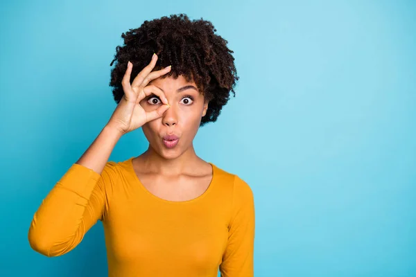 Retrato de chica afro americana loca asombrada hacer signo de bien ojo binocular ver a sus vecinos impresionados mirada estupor desgaste pulóver brillante aislado sobre fondo de color azul —  Fotos de Stock