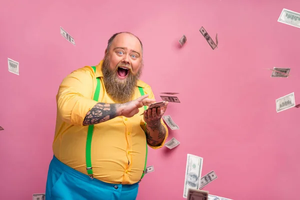 Portré az ő szép vidám vidám vidám boldog izgatott szakállas fickó dobott befektetés nyertes cashback szórakozás minket dollár repül elszigetelt felett rózsaszín pasztell szín háttér — Stock Fotó