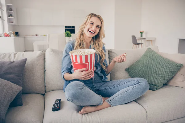 Foto af smukke barfodet dame afslappende sidder komfortabel sofa spise popcorn ben krydsede se komedie romantisk film positive følelser ophold hjem karantæne tid stue indendørs - Stock-foto