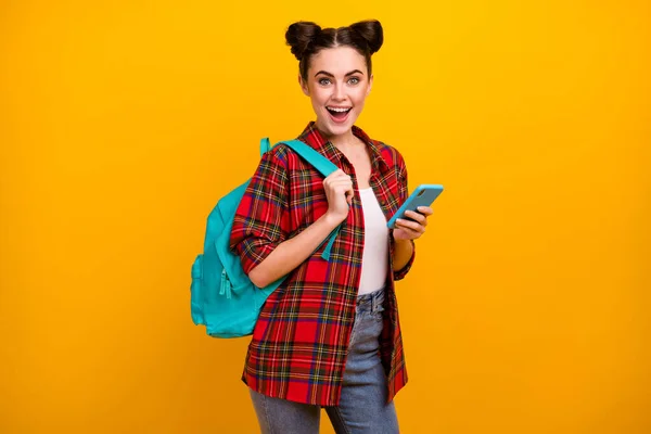 Photo of beautiful amazed student lady hold telephone combine freelance work study read salary income email wear bag casual checkered shirt jeans isolated yellow color background — Stock Photo, Image