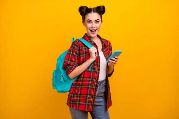 Foto de bela senhora estudante surpreso segurar telefone combinar trabalho freelance estudo ler salário renda e-mail desgaste saco casual camisa xadrez jeans isolado cor amarela fundo — Fotografia de Stock