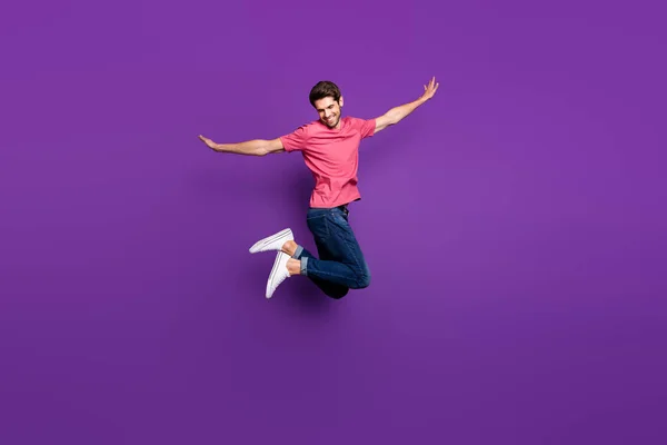 Full Size Profilfoto von hübschen attraktiven Kerl springen hoch oben ausgebreitete Arme Tanz bewegt Flug tragen lässige rosa T-Shirt Jeans Schuhe isoliert lila Farbe Hintergrund — Stockfoto