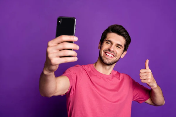 Foto de cara atraente bonito jovem millennial segurar telefone blogger tirar selfies para o novo post levantar o dedo dedo para cima desgaste casual rosa t-shirt isolado cor roxa fundo — Fotografia de Stock