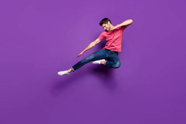 Ganzes Foto von gut aussehenden attraktiven Kerl springen hoch ausgebreitete Arme tanzen seltsame Klecks bewegt tragen lässige rosa T-Shirt Jeans Schuhe isoliert lila Farbe Hintergrund — Stockfoto