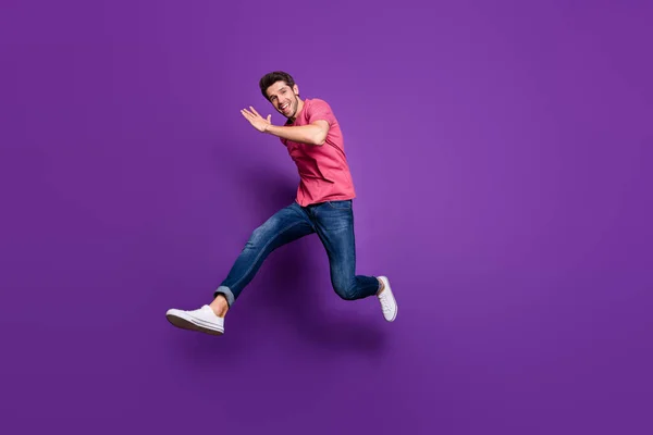 フル長さプロフィール写真のハンサムな魅力的な男ジャンプ高アップ実行しているショッピングセンター販売価格はカジュアルピンクtシャツジーンズの靴を着用絶縁紫の色の背景 — ストック写真