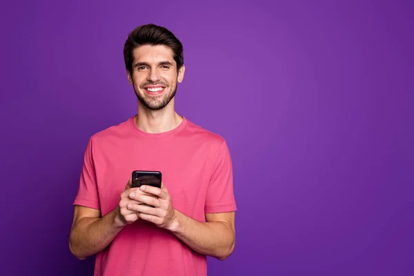 ハンサムな魅力的な男の写真若い千年紀のホールド電話手人気のブロガー中毒ユーザーはカジュアルなピンクのTシャツ孤立紫の色の背景を着用 — ストック写真